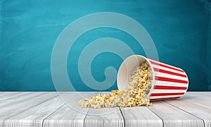 3d rendering of popcorn bucket lying sidelong with some popcorn spilled on wooden surface near blue wall with copy space