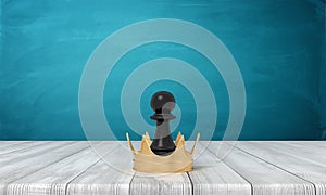 3d rendering of a small black chess pawn standing inside a golden crown on a wooden desk background.