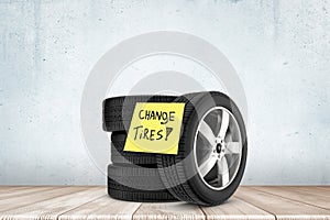 3d rendering of stack of black tires with yellow post-it note saying `Change Tires`, against concrete wall on wooden