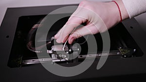 3D technology two men`s hands push a plastic white thread into prongs of printer