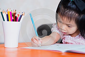 A 4-5 year old Asian girl is working hard on her assignment. Children sit and write homework. Children study at home.