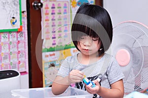 A 4-5 year old cute Asian girl is sitting with plastic blocks in her bedroom in a cozy house. Little child use their hand muscles