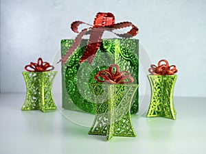 4 green metallic Christmas presents with red bows on top, sitting on a white counter.  Red and green Christmas holiday decor.