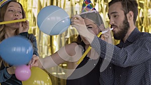 4 happy cheerful people at a party in paper caps fighting balloons. The guys are blowing in the pipes and dancing. A