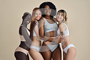 4 happy diverse young girls in underwear hugging isolated on beige background.