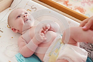 4 months old infant boy lying on changing desk, mother hands holding his legs