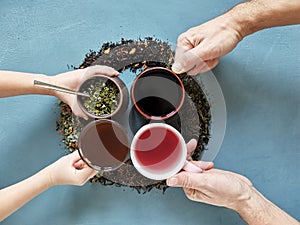 4 mugs with different types of tea and four hands