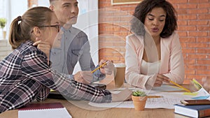 4 people are a group of people of mixed race. young guys are discussing a project at a round table pointing to a drawing