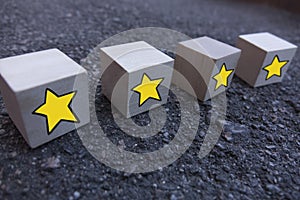 4 wooden cubes with a pattern of a yellow star standing on top of each other on asphalt