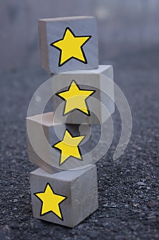 4 wooden cubes with a pattern of a yellow star standing on top of each other on asphalt