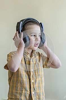 A 4 year boy in a shirt attentively listens to music in big black headphones. Little boy listening to music in big black headphone