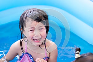 4-year-old Asian girl is crying in blue pool while playing in water and there is accident in water play activities at home.