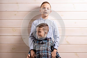 A 4-year-old boy in a blue klepy shirt cries on a light wooden background and his brother, 10 years old, is standing