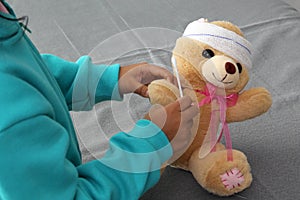 4-year-old brunette Latina girl with glasses represents mistreatment and physical abuse in her teddy bear with bandages on her hea