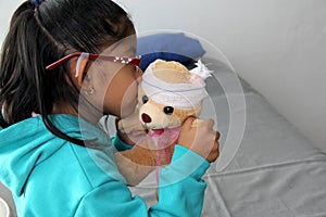 4-year-old brunette Latina girl with glasses represents mistreatment and physical abuse in her teddy bear with bandages on her hea