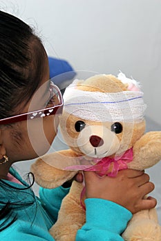 4-year-old brunette Latina girl with glasses represents mistreatment and physical abuse in her teddy bear with bandages on her hea