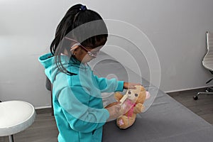 4-year-old brunette Latina girl with glasses represents mistreatment and physical abuse in her teddy bear with bandages on her hea