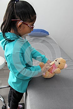 4-year-old brunette Latina girl with glasses represents mistreatment and physical abuse in her teddy bear with bandages on her hea