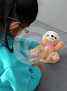 4-year-old brunette Latina girl with glasses represents mistreatment and physical abuse in her teddy bear with bandages on her hea