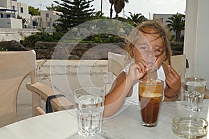 4 year old girl drinks decaffeinated coffee frappe during her holidays in Greece