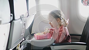 4 year old girl eating snacks from lunch box while travelling by plane. Healthy food for kids during flight