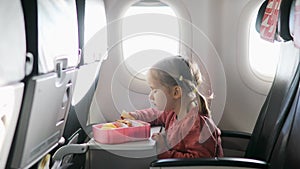 4 year old girl eating snacks from lunch box while travelling by plane. Healthy food for kids during flight