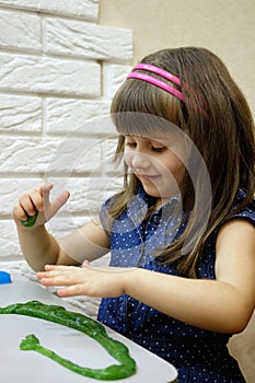 A 4-year-old girl plays with bright green glitter slime. This activity promotes the development of fine motor skills, creative