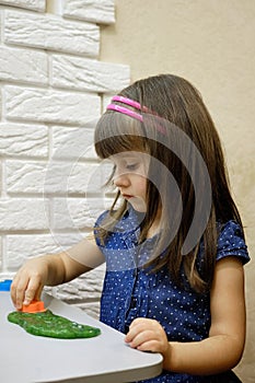 A 4-year-old girl plays with bright green glitter slime. This activity promotes the development of fine motor skills, creative