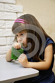 A 4-year-old girl plays with bright green glitter slime. This activity promotes the development of fine motor skills, creative