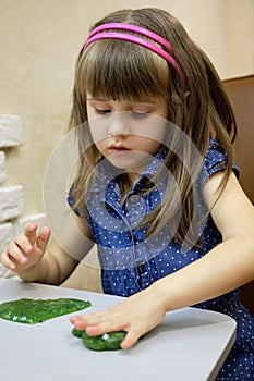 A 4-year-old girl plays with bright green glitter slime. This activity promotes the development of fine motor skills, creative