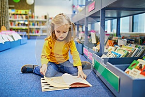 4 year old girl sitting on the floor in a municipal library and reading a book