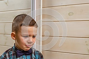 A 4 years old boy in a blue clerical shirt is crying on a light wooden background