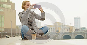 40-year-old beautiful woman taking a photo of cityskape with her smartphone during coffee break.
