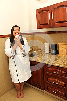 40-year-old Latina woman in a bathrobe drinks a cup of coffee in her kitchen to avoid diabetes, parkinson\'s and depression