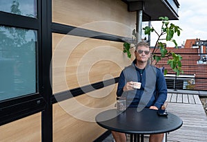 40 year old white man with sungasses, drinking coffee on the terrace of his apartment