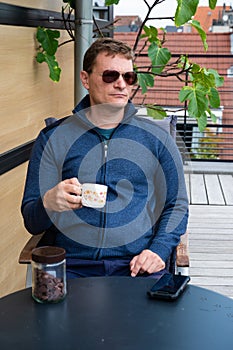 40 year old white man with sungasses, drinking coffee on the terrace of his apartment