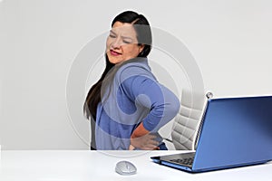 40-year-old woman suffers from back, neck and head pain due to stress and burnout while working in her office with her laptop