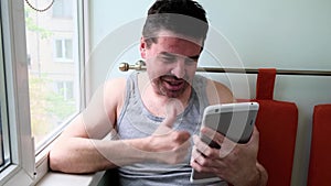 40 years old middle age man sitting at home near a window, talking to tablet pc, using wireless internet connection.
