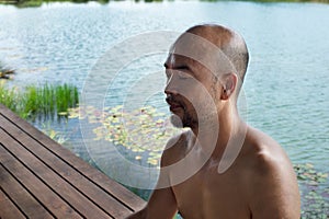 40s bald beard man eye closing mediation with summer blue water lake in wellness relaxation background