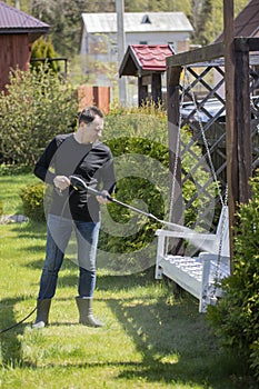 40s man washes white swings in country house garden with high pressure washer