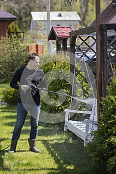 40s man washing wooden swings in country house garden with high pressure washer