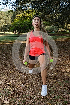 42 year old Brazilian woman doing stationary lunges with dumbells in a public square front view