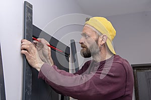 45-50-year-old male construction worker MARKS out the trim on the wooden doors with a PENCIL; Concept: interior decoration, constr