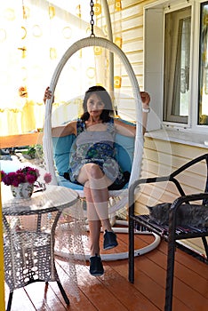 45 years old Russian woman resting on hanging swing chair on cozy veranda with slepping cat