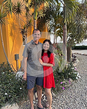 47 year-old Caucasian husband and his 57 year-old Korean wife posing in a garden in Cabo San Lucas.