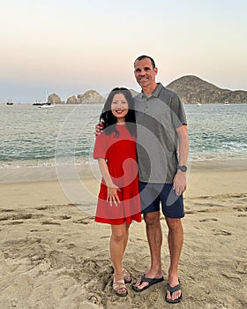 47 year-old Caucasian husband and his 57 year-old Korean wife posing on Medano Beach in Cabo San Lucas.