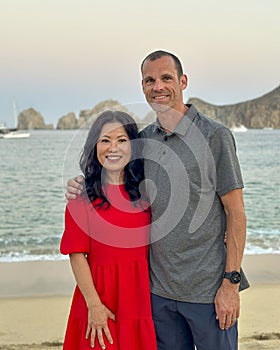 47 year-old Caucasian husband and his 57 year-old Korean wife posing on Medano Beach in Cabo San Lucas.