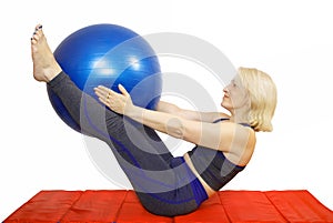 A 48-year-old woman performs an exercise from a Pilates course compresses kicking the ball the fitball and raises them