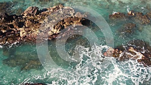 4K aerial shot from a drone from above, the purest turquoise waters break on the rocks near the shore and foam. Surf