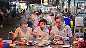 4K Asian family enjoy eating food on street food restaurant with crowd of people at Yaowarat road